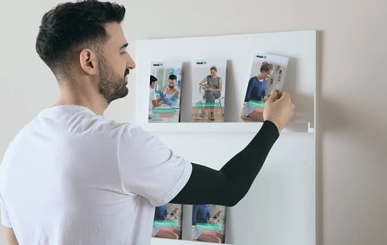 Young male patient wearing a black compression sleeve, looking at a Juzo catalog stand.