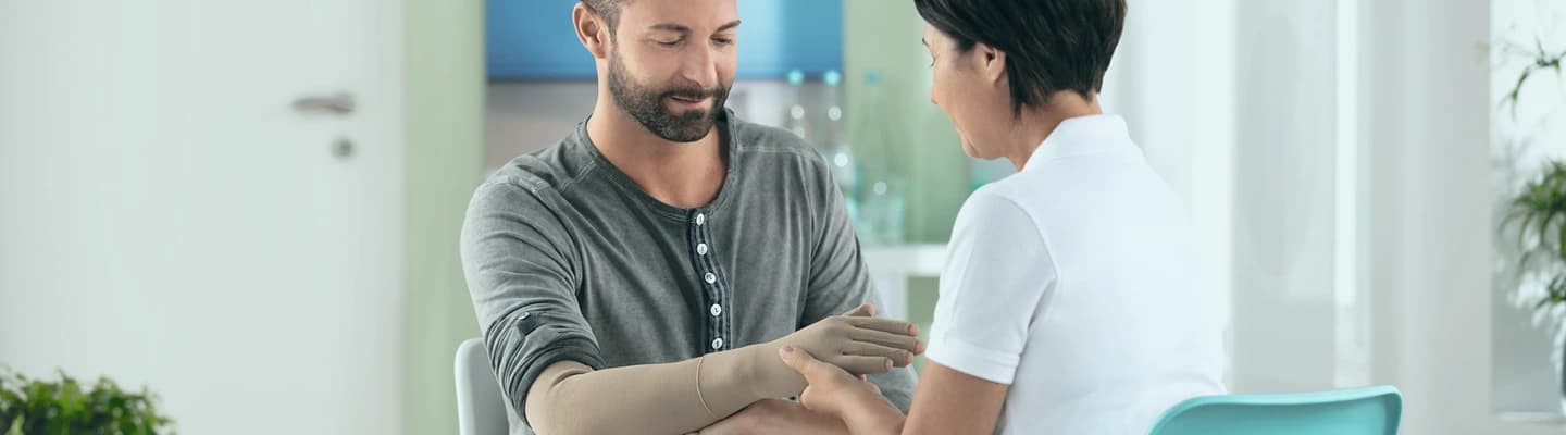 Juzo expert assisting a patient wearing a compression glove and compression sleeve at clinic.